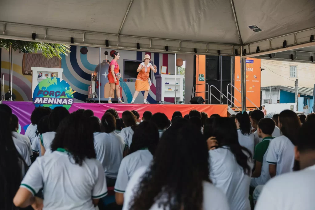 Um grupo de jovens sentadas em uma tenda assistindo a peça teatral