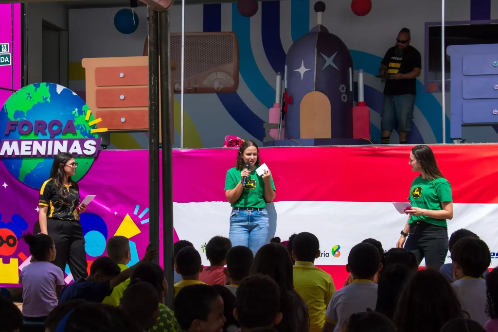 3 mulheres em um palco falando sobre suas experiências para uma multidão de alunos