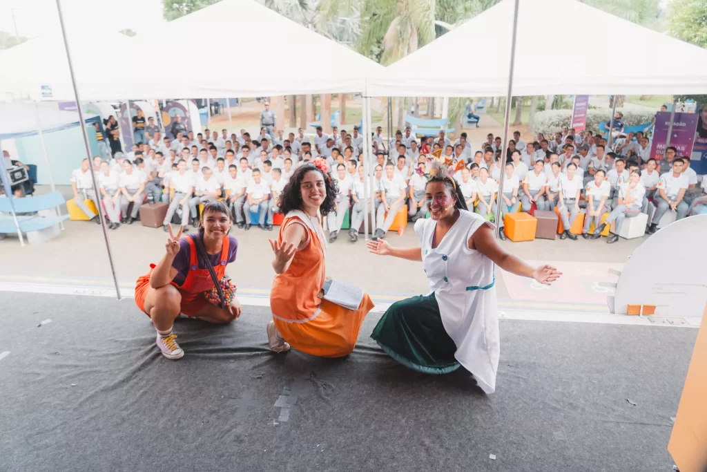 Atrizes posando para uma foto em cima do palco com plateia jovem