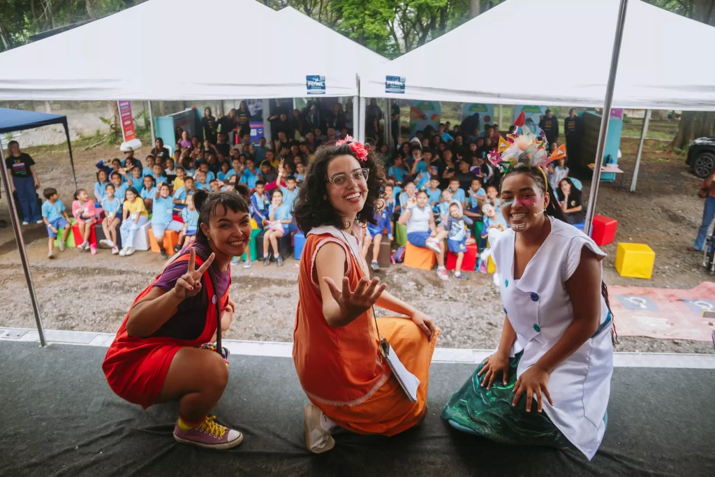 Atrizes posando para foto em cima do palco com publico jovem